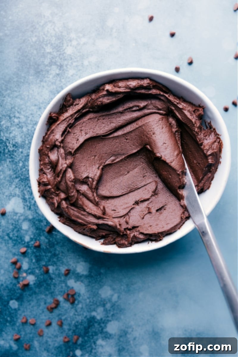 The Best Chocolate Buttercream Frosting is deeply chocolate, rich, luscious, and smooth. This American-style buttercream is an indulgent treat! Perfect for cakes, cupcakes, and any dessert. Chocolate Buttercream Frosting Recipe in a bowl with a butter knife scooping some out.