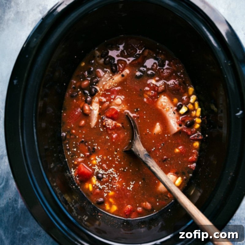 All the vibrant ingredients for the Crockpot Quinoa Chili are now mixed and combined within the slow cooker, perfectly arranged and ready to begin the cooking process.