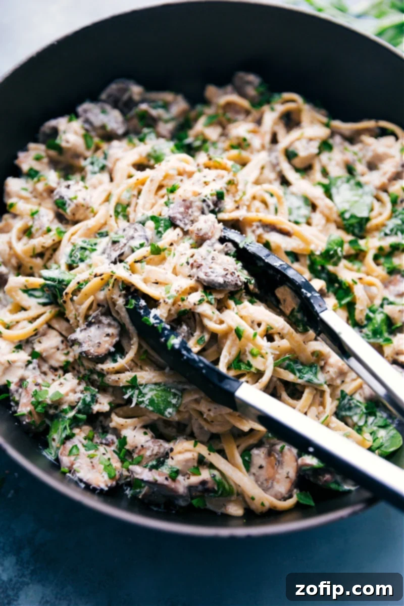 Creamy chicken pasta in a skillet with a big spoonful being lifted out to serve, showing the rich sauce and fresh ingredients.