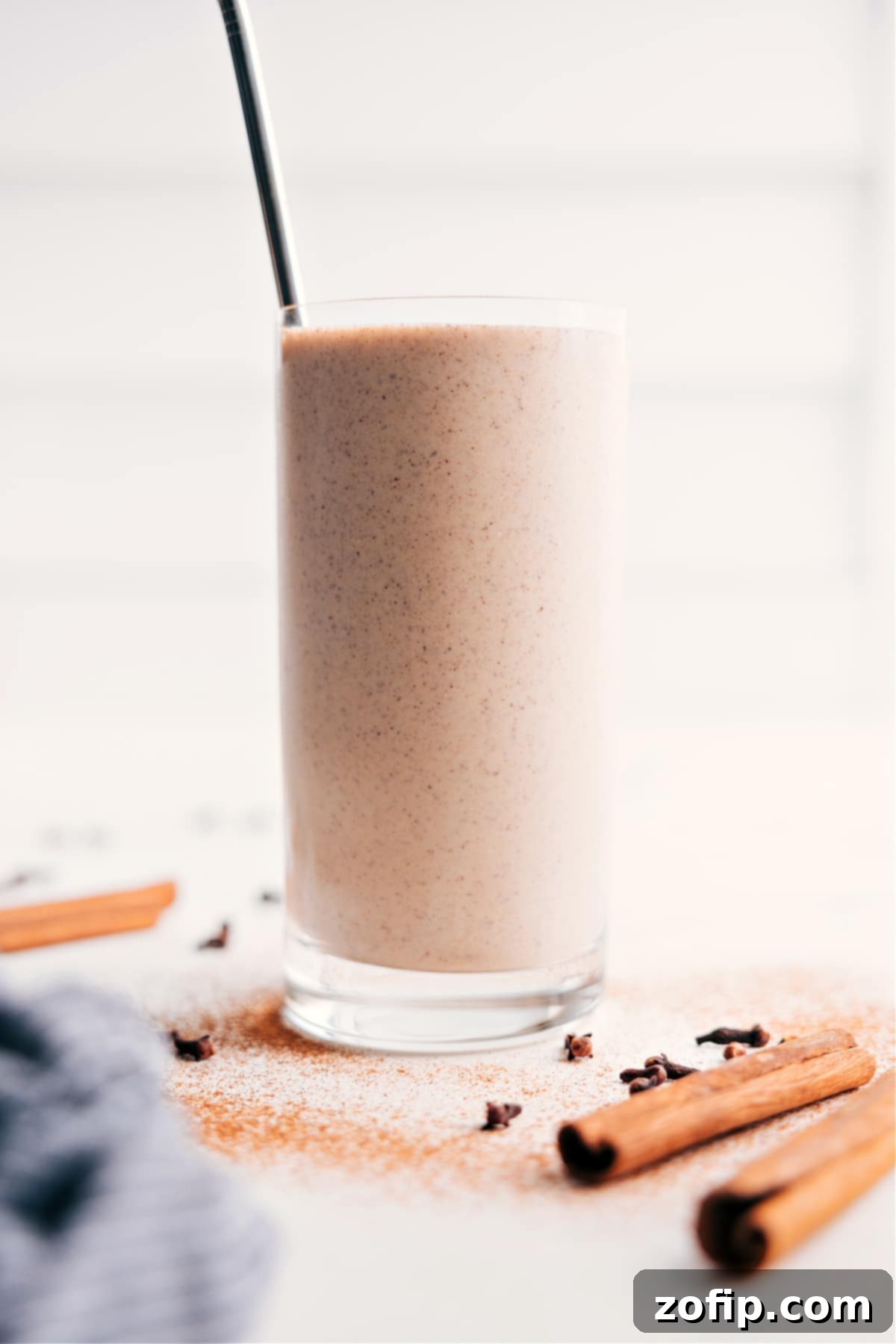 A tall glass of creamy and delicious homemade chai smoothie, garnished with a light sprinkle of cinnamon, ready to be enjoyed. The drink is frosty and rich with warm, inviting colors.
