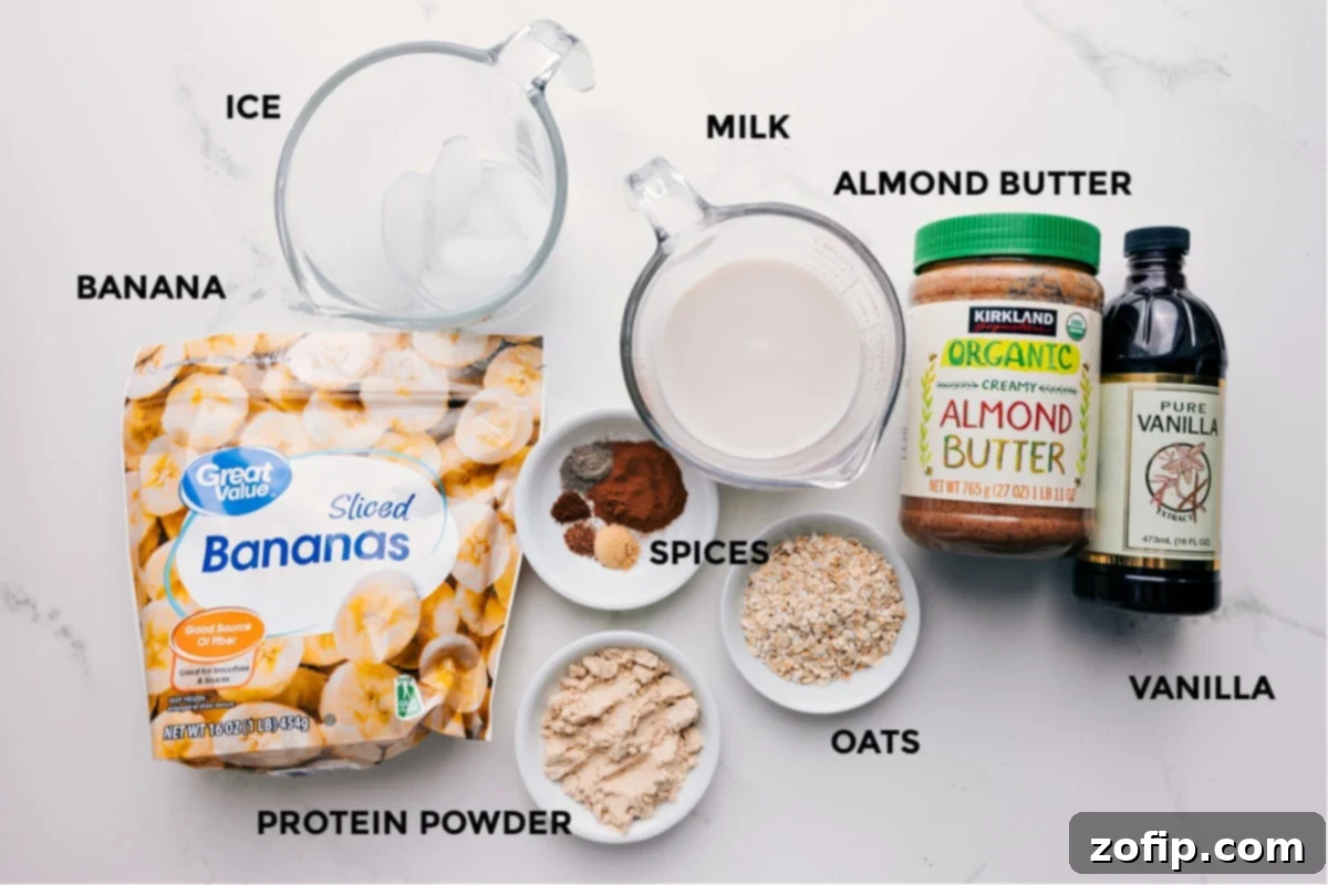 All the fresh and carefully prepped ingredients for the homemade chai smoothie recipe laid out on a clean surface. The spread includes plant-based milk, perfectly sliced frozen banana coins, whole old-fashioned oats, creamy almond butter, clear vanilla extract, a vibrant mix of ground chai spices (cinnamon, ginger, cardamom, nutmeg, and cloves), a scoop of vanilla protein powder, and sparkling ice cubes.