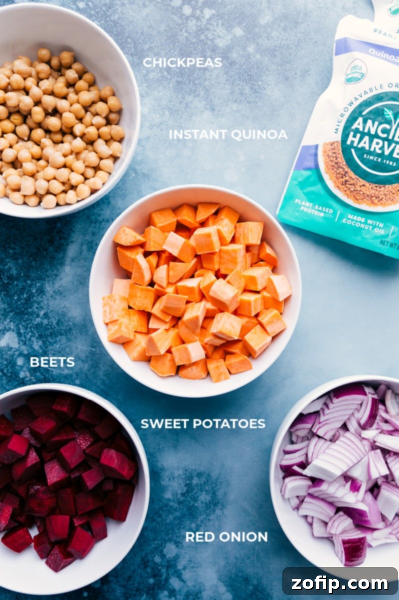 A close-up shot of the main ingredients for Sheet Pan Quinoa Pilaf laid out, including colorful beets, sweet potatoes, red onion, chickpeas, and packets of microwaveable quinoa.