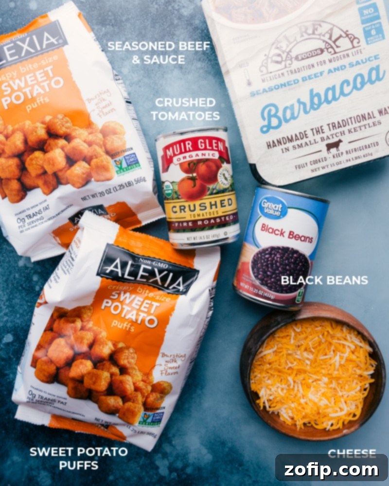 All ingredients for Deconstructed Beef Totchos laid out: sweet potato puffs, barbacoa beef, black beans, fire-roasted tomatoes, cheese, avocado, sour cream, lime, cilantro