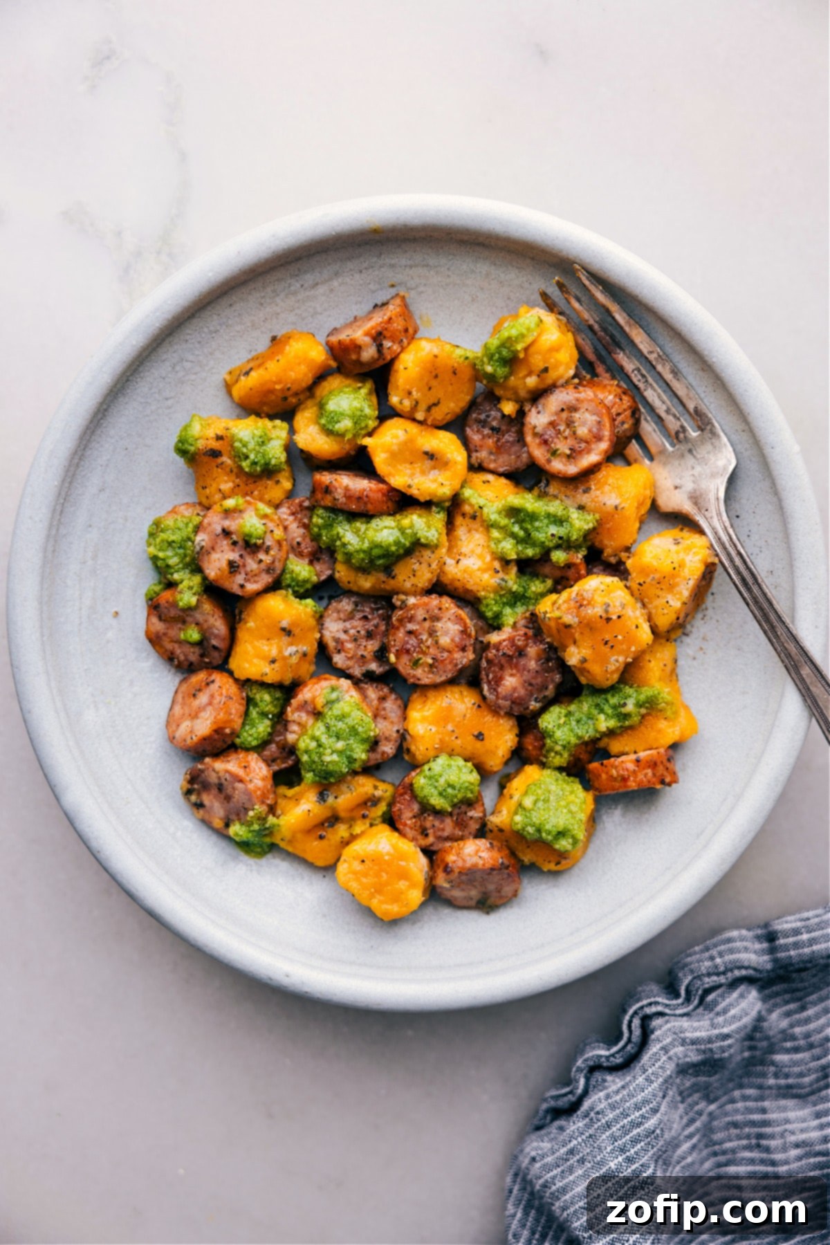 A serving of roasted sweet potato gnocchi and Italian chicken sausage with fresh basil pesto on a plate