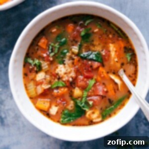 A bowl of hearty crockpot chicken quinoa soup, with chicken, quinoa, vegetables, and herbs.