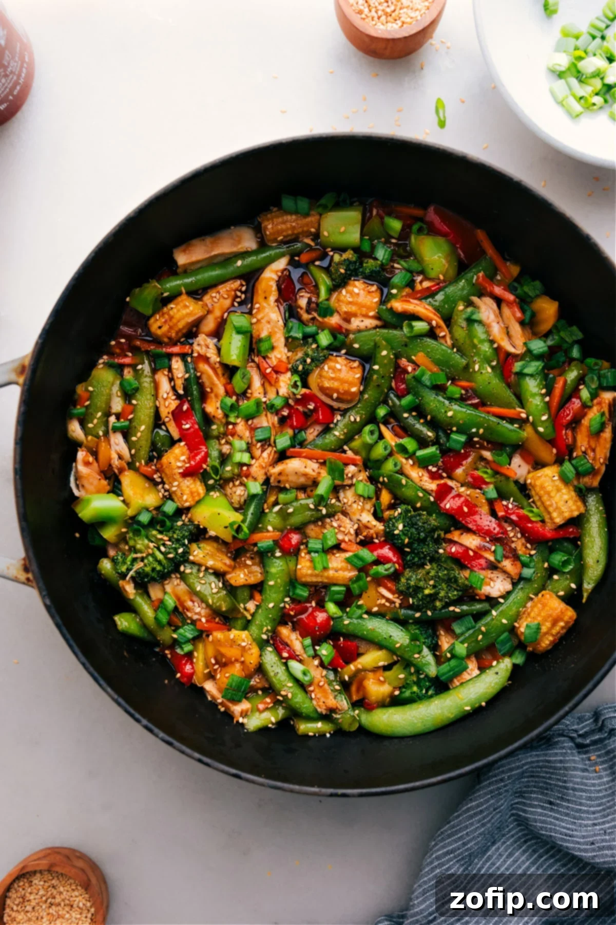 Delicious Rotisserie Chicken Stir-Fry in a wok, garnished with fresh green onions and sesame seeds, ready to be served over rice.