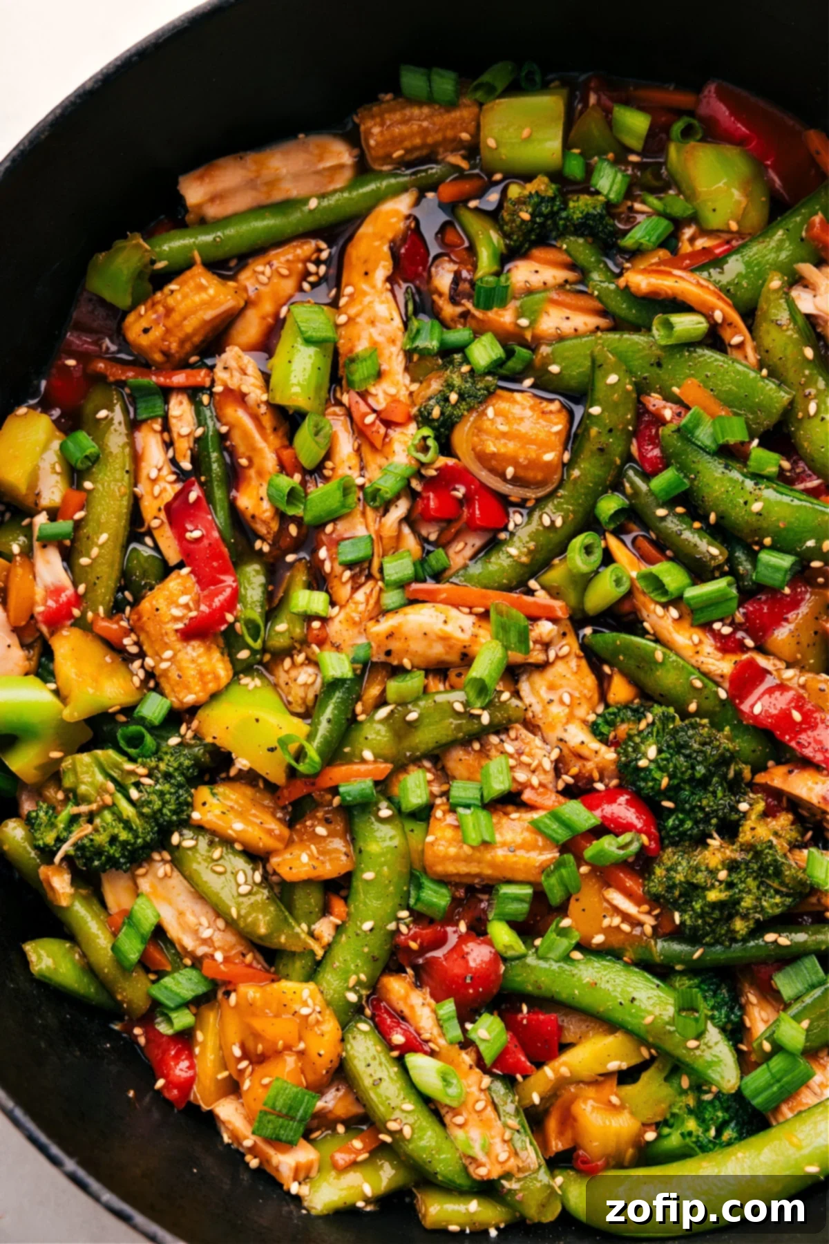 The finished rotisserie chicken stir-fry, glistening with its rich sauce, resting in a large skillet, beautifully garnished and ready to be served immediately.