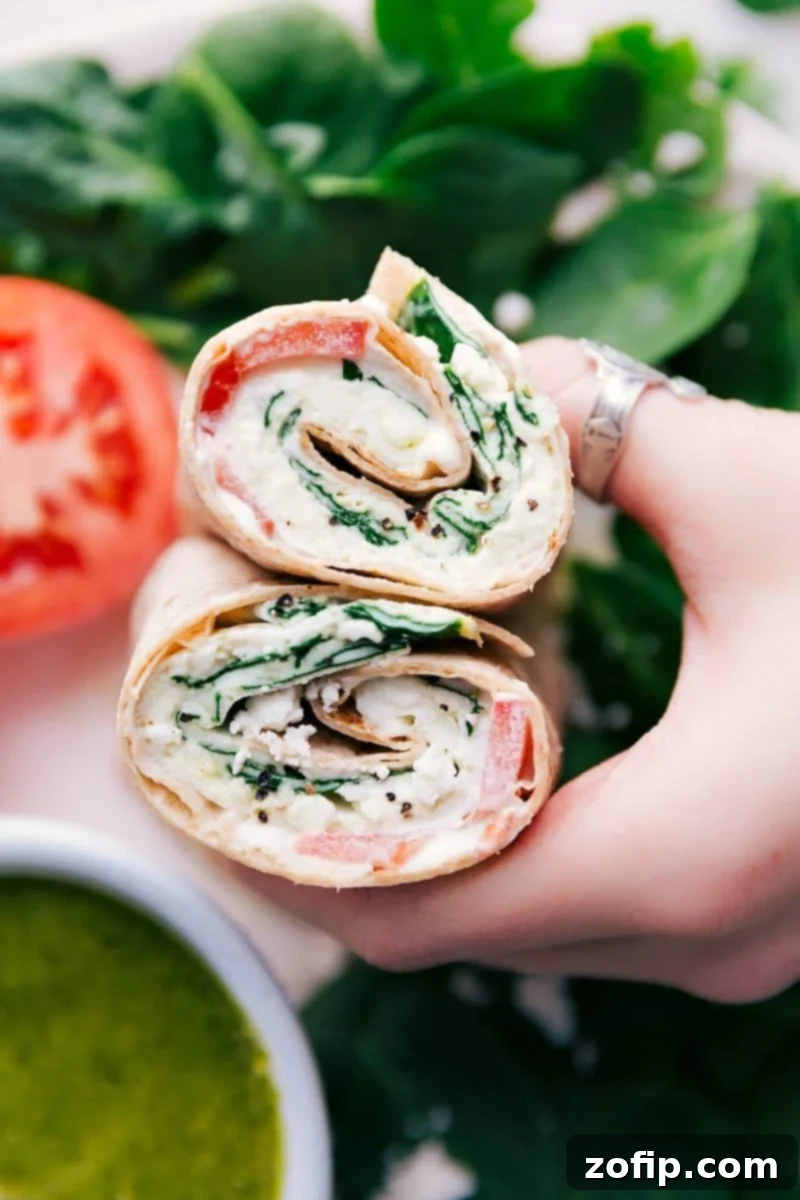 A perfectly cut whole wheat egg wrap, showcasing a vibrant filling of fluffy egg whites, fresh spinach, tangy feta, rich pesto, and juicy tomatoes, ready to be enjoyed.