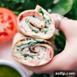 A perfectly cut whole wheat egg wrap, showcasing a vibrant filling of fluffy egg whites, fresh spinach, tangy feta, rich pesto, and juicy tomatoes, ready to be enjoyed.