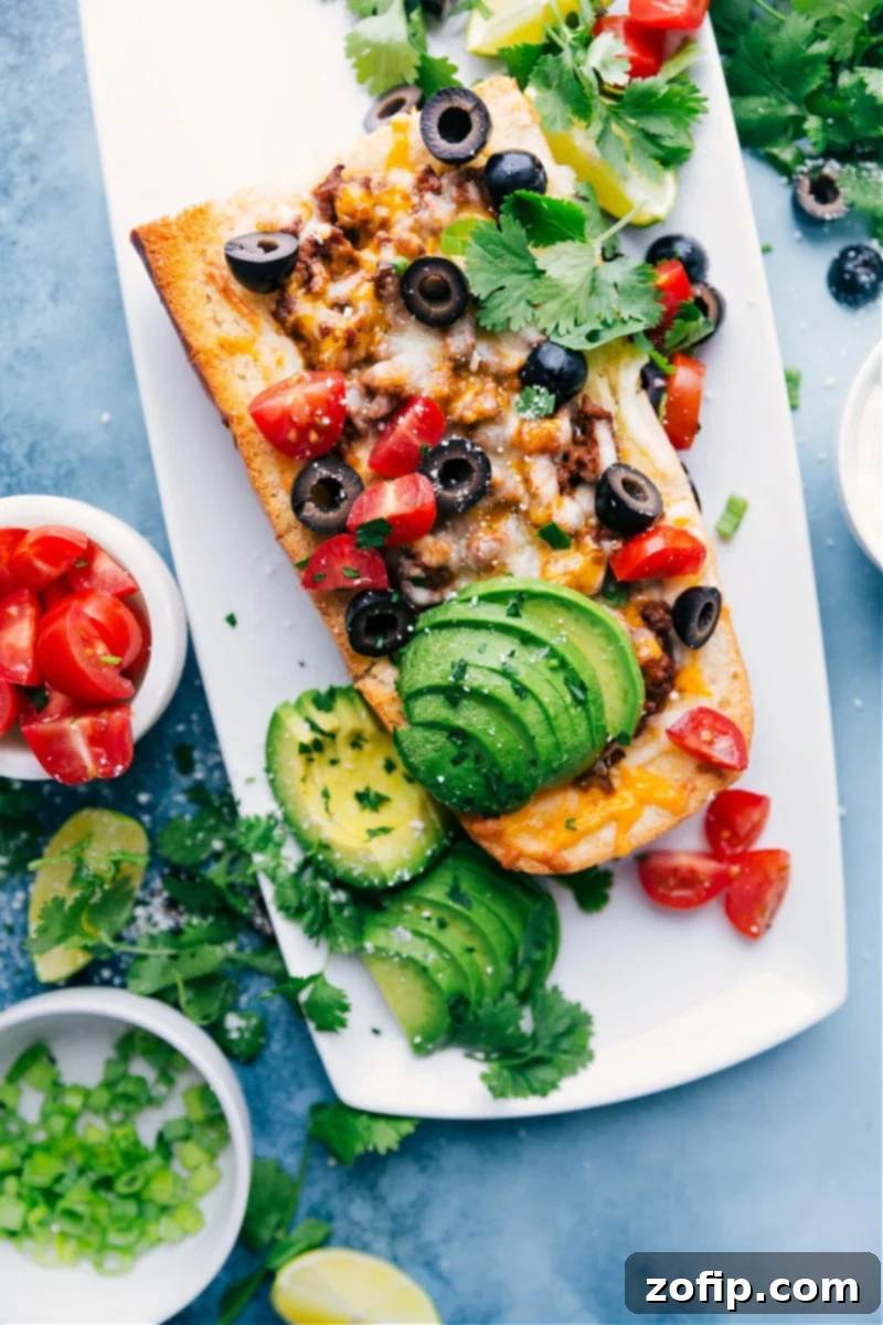 A delicious French Bread Taco Pizza, generously topped with seasoned meat, melted cheese, and fresh ingredients like cilantro and tomatoes, presented on a wooden board.