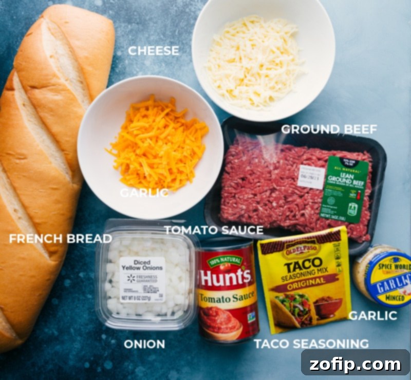 All the fresh ingredients laid out for French Bread Taco Pizza, including a loaf of French bread, ground beef, cheese, onions, garlic, tomato sauce, and taco seasoning.