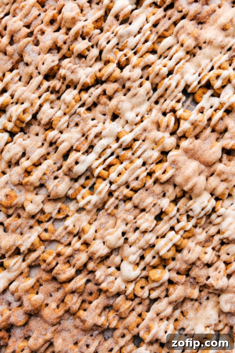 Sweet Churro Cheerios! It's an explosion of churro flavor with a totally addictive, crunchy texture and just the right amount of sweetness! Recipe via ChelseasMessyApron.com #sweettooth #snackgoals #churrocereal #deliciouslyaddictive A close-up image of the finished Churro Cheerios in a bowl, showcasing their golden caramel coating, delicate white chocolate drizzle, and sparkling cinnamon-sugar crust.