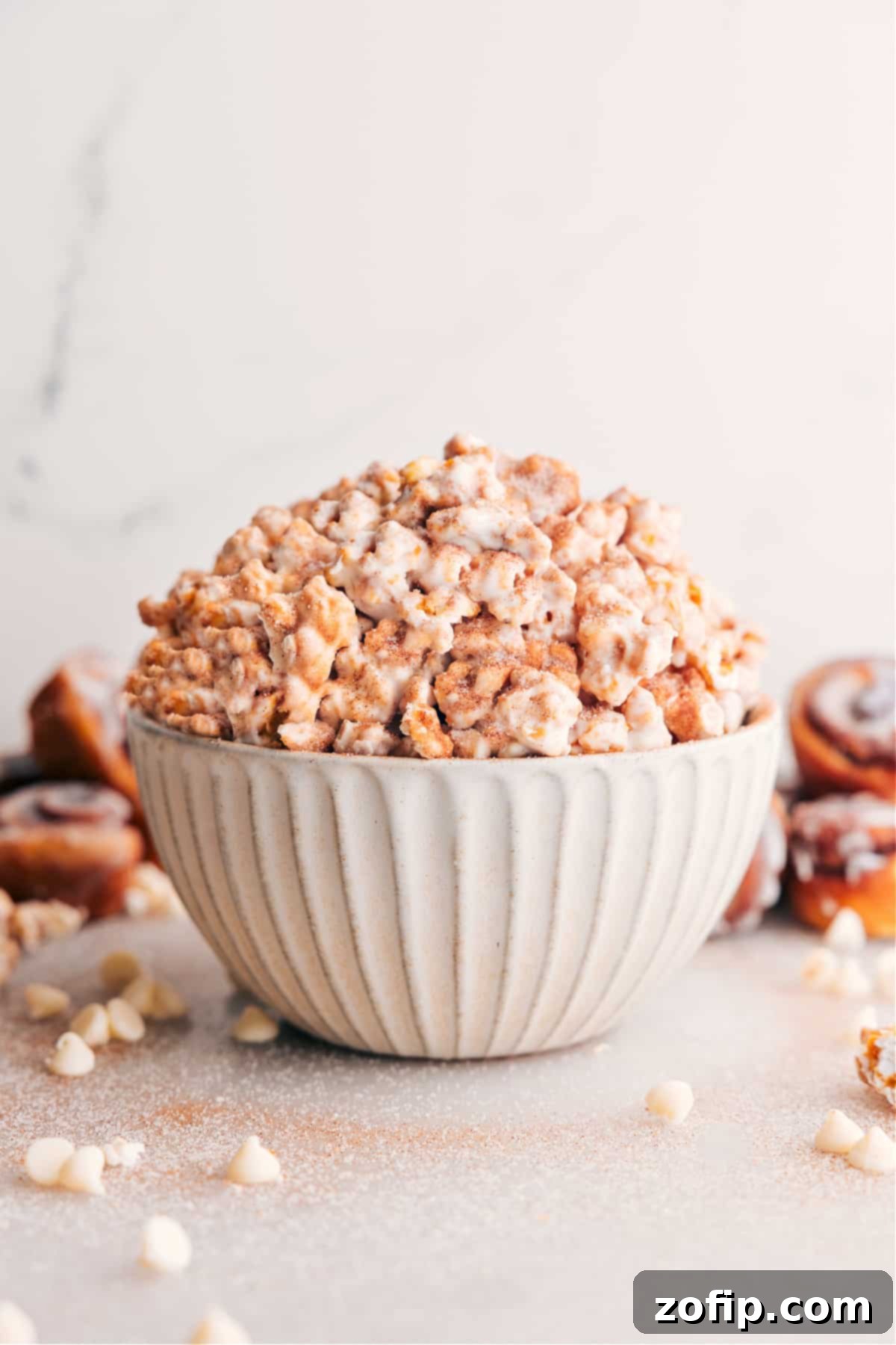 A large, inviting bowl filled to the brim with golden Cinnamon Roll Popcorn, glistening with caramel and delicate white chocolate drizzles, generously sprinkled with cinnamon sugar, ready for serving and enjoyment.
