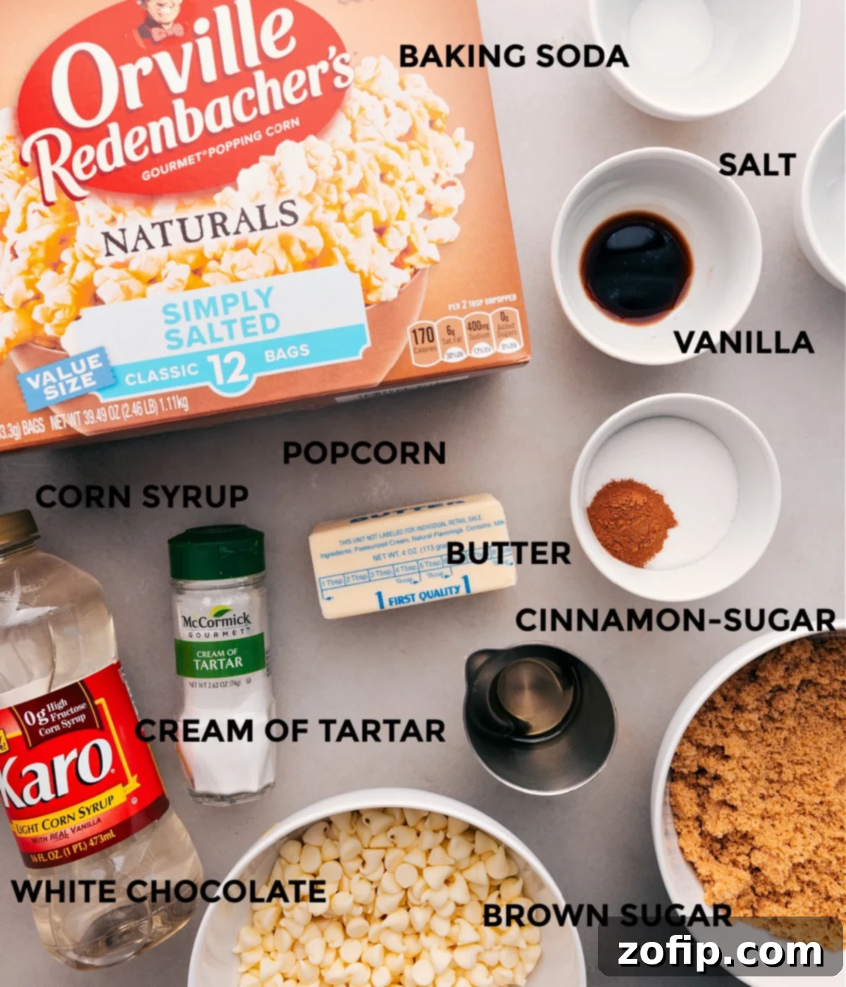 A beautifully arranged spread of all the high-quality ingredients required for crafting perfect Cinnamon Roll Popcorn: fluffy popped popcorn, baking soda, fine sea salt, aromatic cinnamon and other spices, cream of tartar, golden light corn syrup, granulated sugar, and luxurious white chocolate chips.