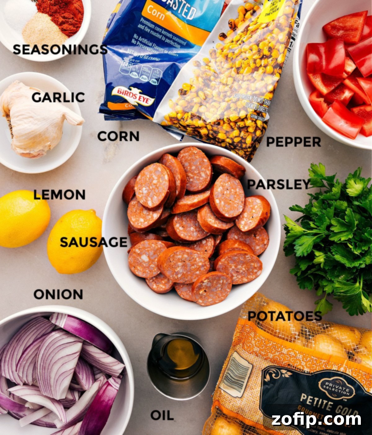 All the essential ingredients meticulously prepped and laid out for making a one-pan smoked sausage and potatoes dinner: sliced sausage, halved baby potatoes, red bell pepper, red onion, frozen corn, garlic, paprika, olive oil, salt, and pepper.