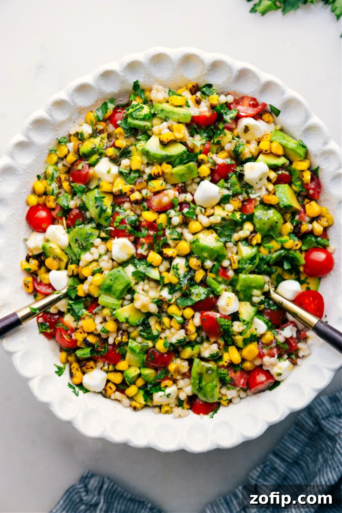 Summer Couscous Salad in a large serving bowl with fresh herbs and a drizzle of dressing, ready to be enjoyed.