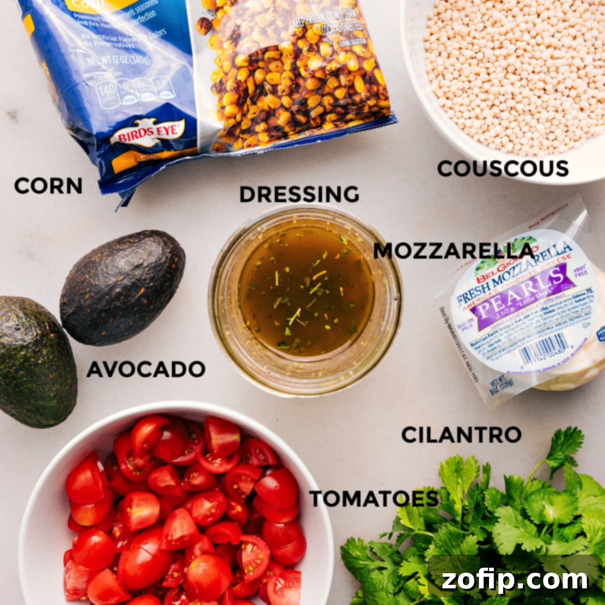 All the fresh ingredients meticulously prepped for easy assembly of the Summer Couscous Salad, including mozzarella, fresh herbs, tomatoes, avocado, dressing, cooked couscous, and roasted corn.