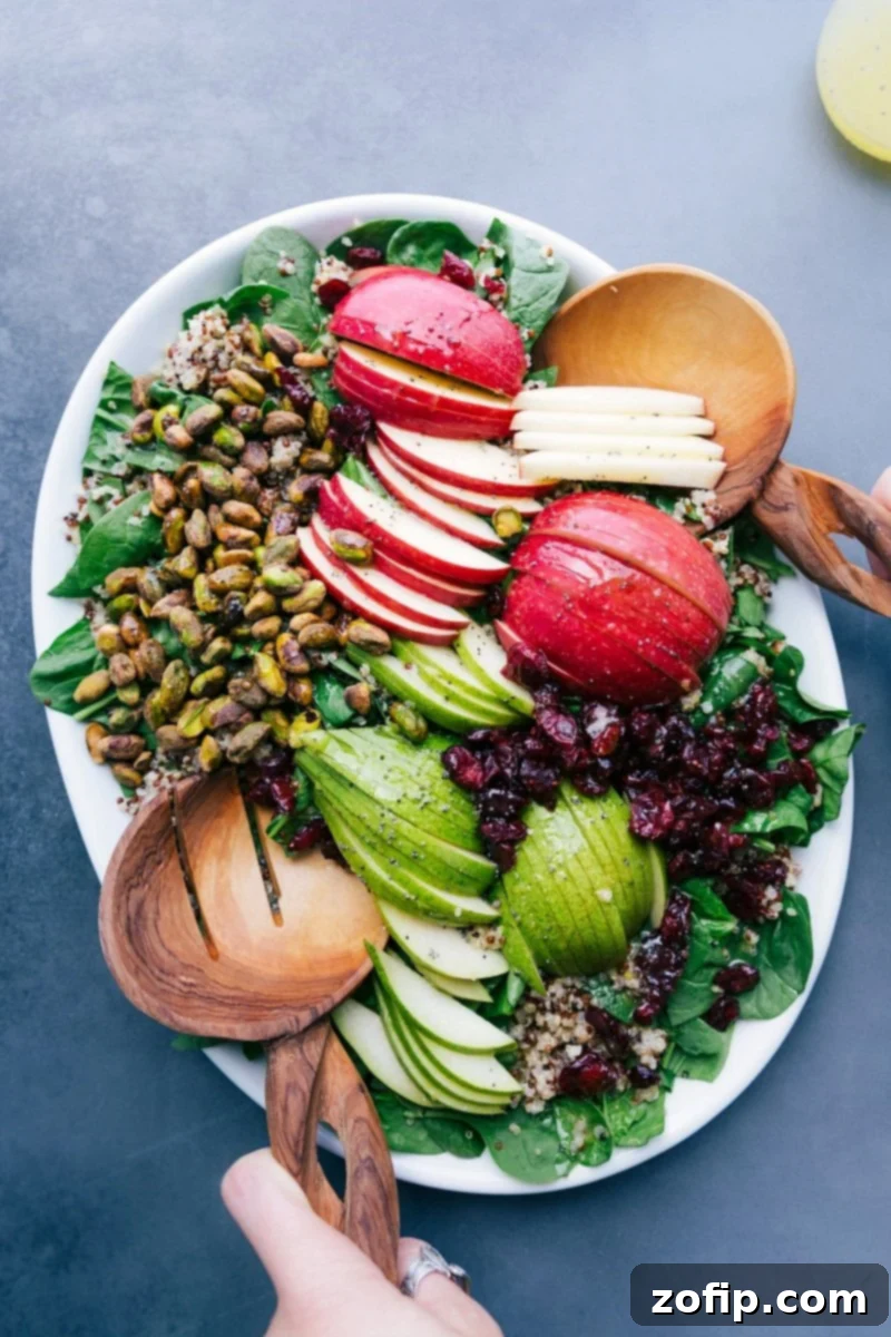 A beautifully arranged Quinoa Apple Salad on a rustic platter, featuring fresh mixed greens, perfectly sliced red apples and green pears, crunchy pistachios, and sweet dried cranberries, all glistening with dressing.
