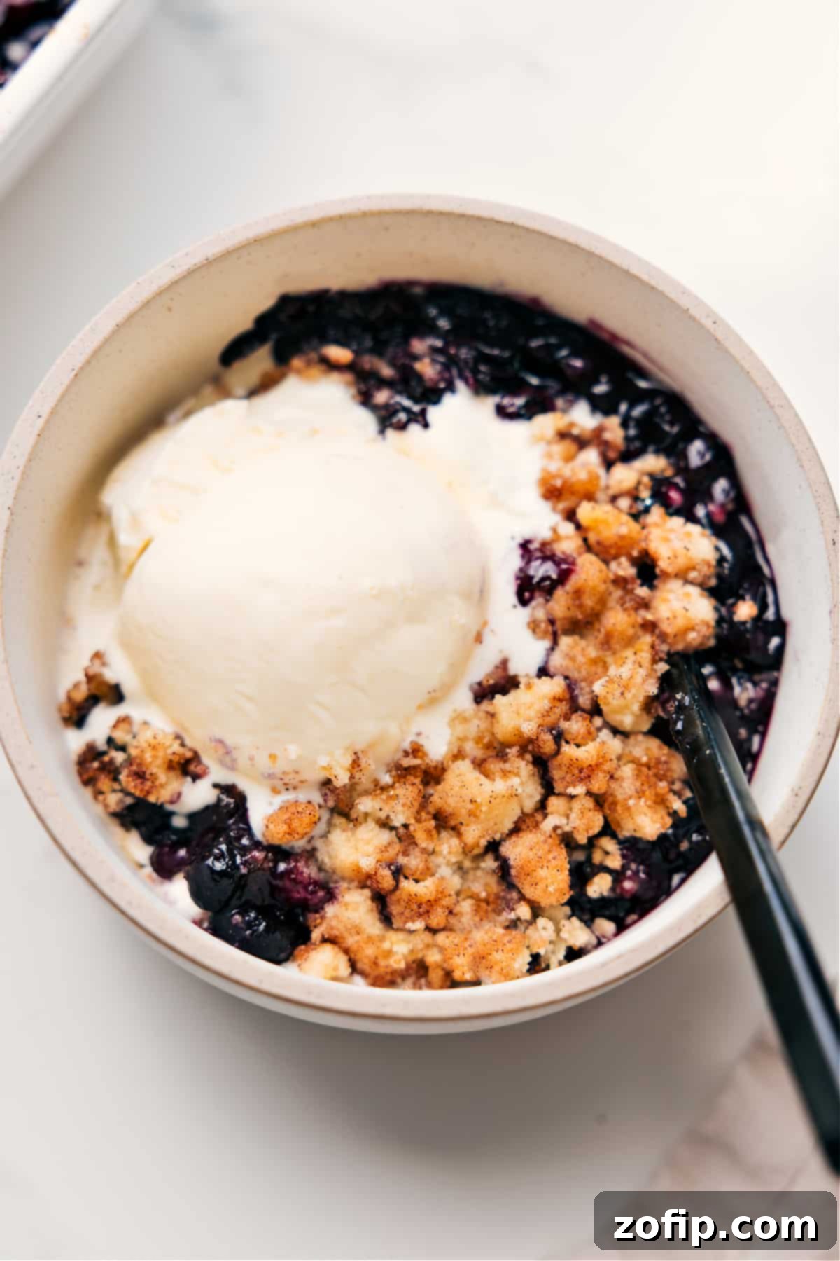Blueberry Cobbler served in a rustic bowl with a generous scoop of melting vanilla ice cream on top, ready to be enjoyed.