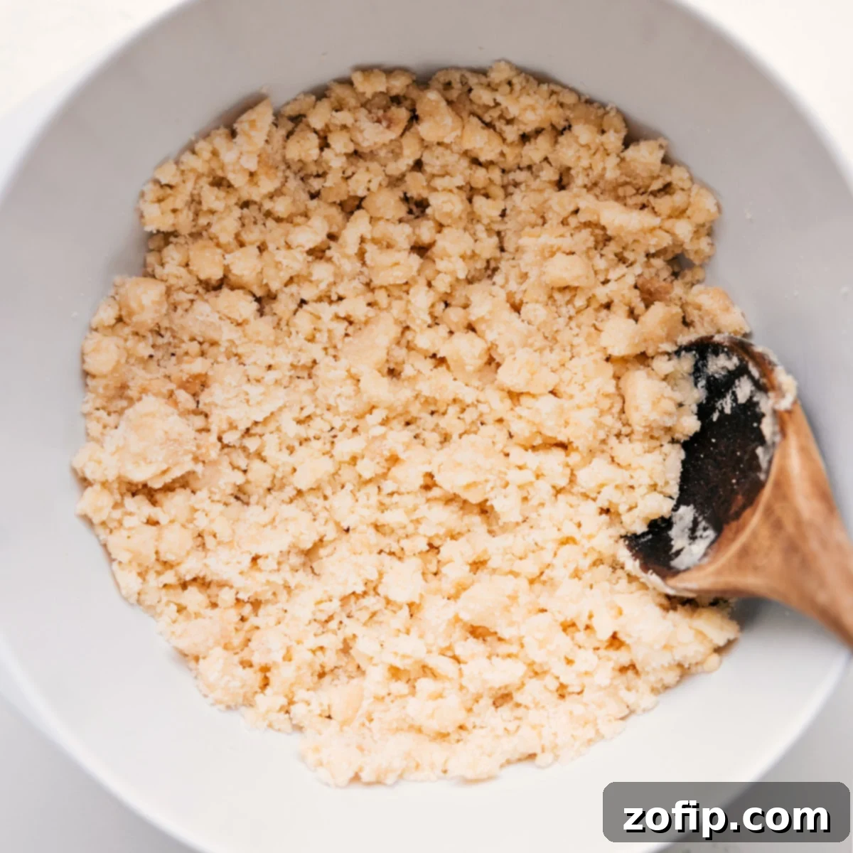 A bowl filled with the golden-brown, crumbly topping mixture for blueberry cobbler, ready to be sprinkled over the fruit.
