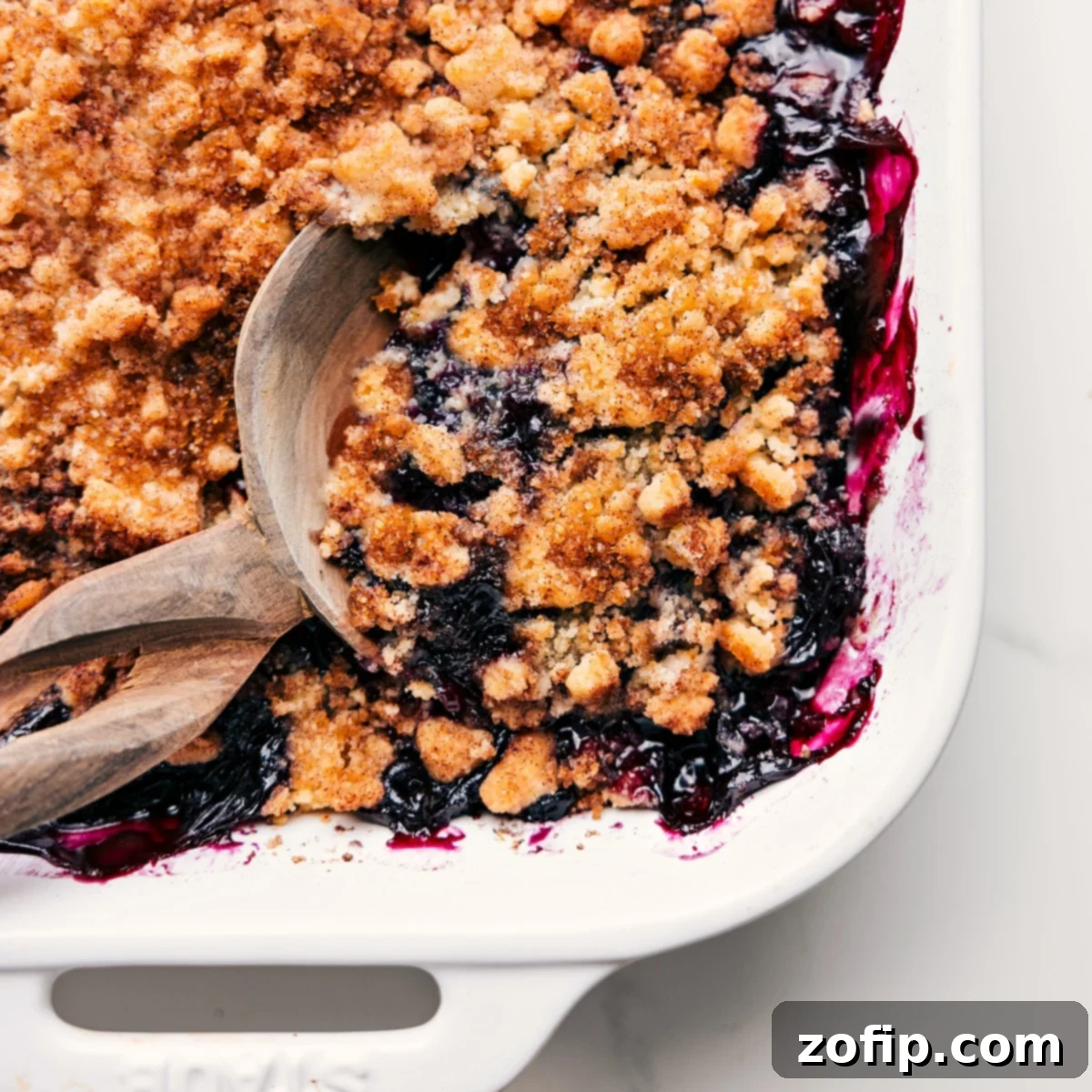 A close-up of a freshly baked blueberry cobbler, golden brown and bubbling, with a serving spoon gently scooping out a portion from the dish.