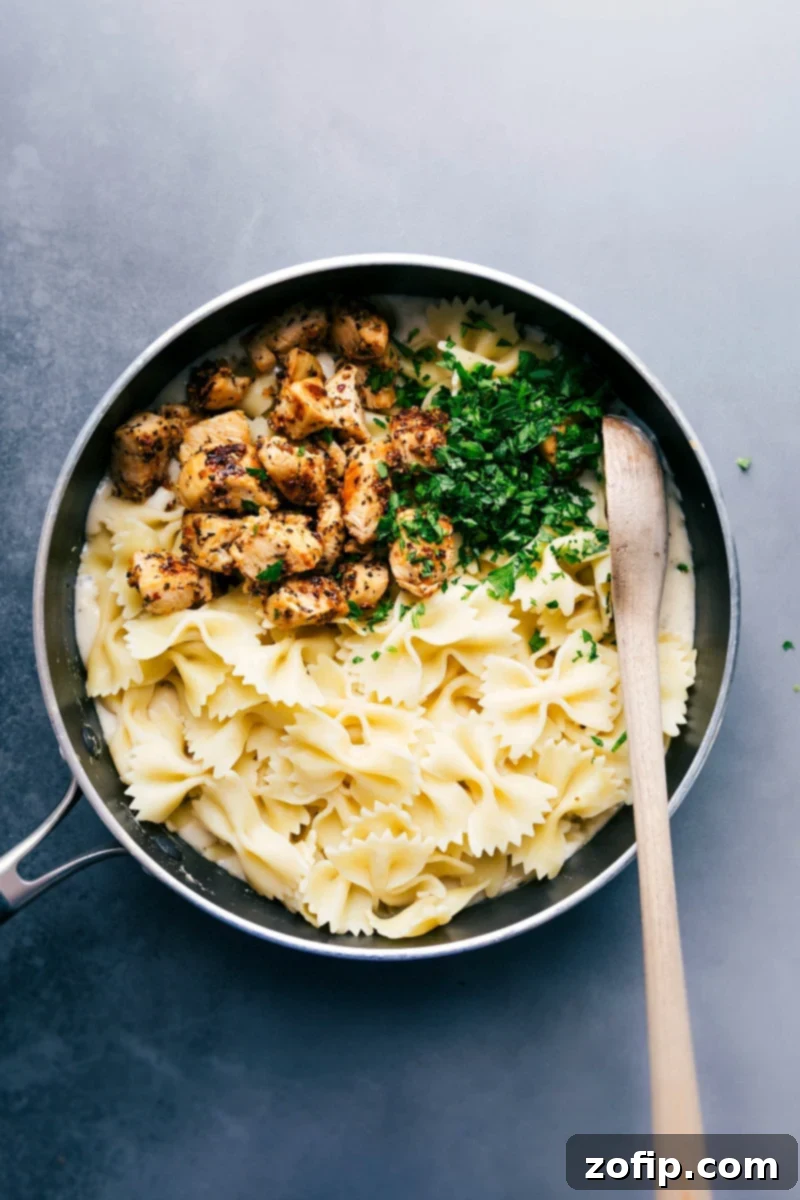 Pasta, chicken, and fresh parsley over the alfredo sauce, about to be mixed together to create a delicious meal.