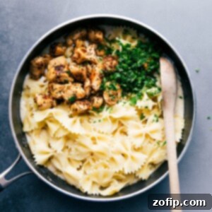 Pasta, chicken, and fresh parsley over the alfredo sauce, about to be mixed together to create a delicious meal.