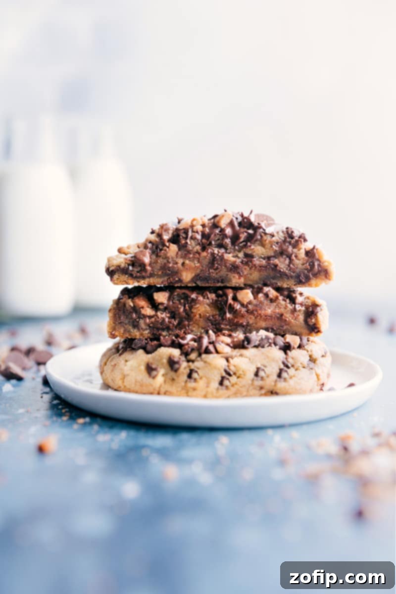 A freshly baked Gideon's Bakehouse style cookie, cut in half to reveal its gooey, chocolate-packed interior, stacked on another whole cookie.