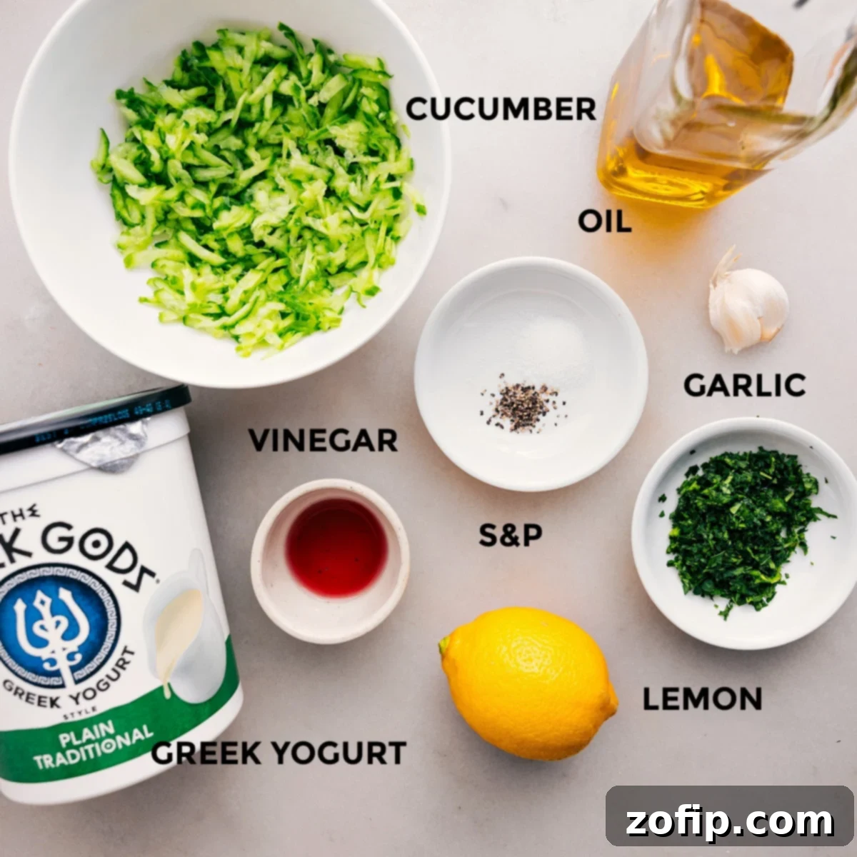 Ingredients In Tzatziki Sauce All the essential ingredients for Tzatziki Sauce are artfully arranged and prepped on a wooden board, including a bowl of Greek yogurt, grated cucumbers, a fresh lemon, garlic cloves, olive oil, red wine vinegar, and a selection of fresh herbs like dill and mint, alongside salt and pepper.