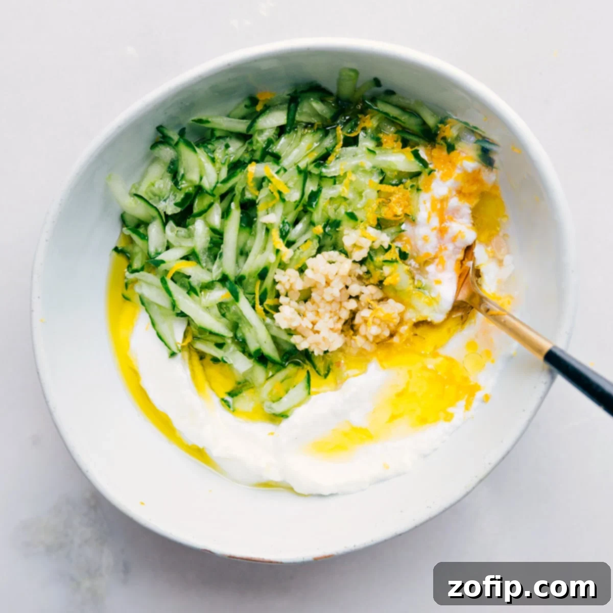 Make Tzatziki Sauce All In One Bowl All the tzatziki sauce ingredients have been added to a single bowl and are being whisked together to create the creamy dip.