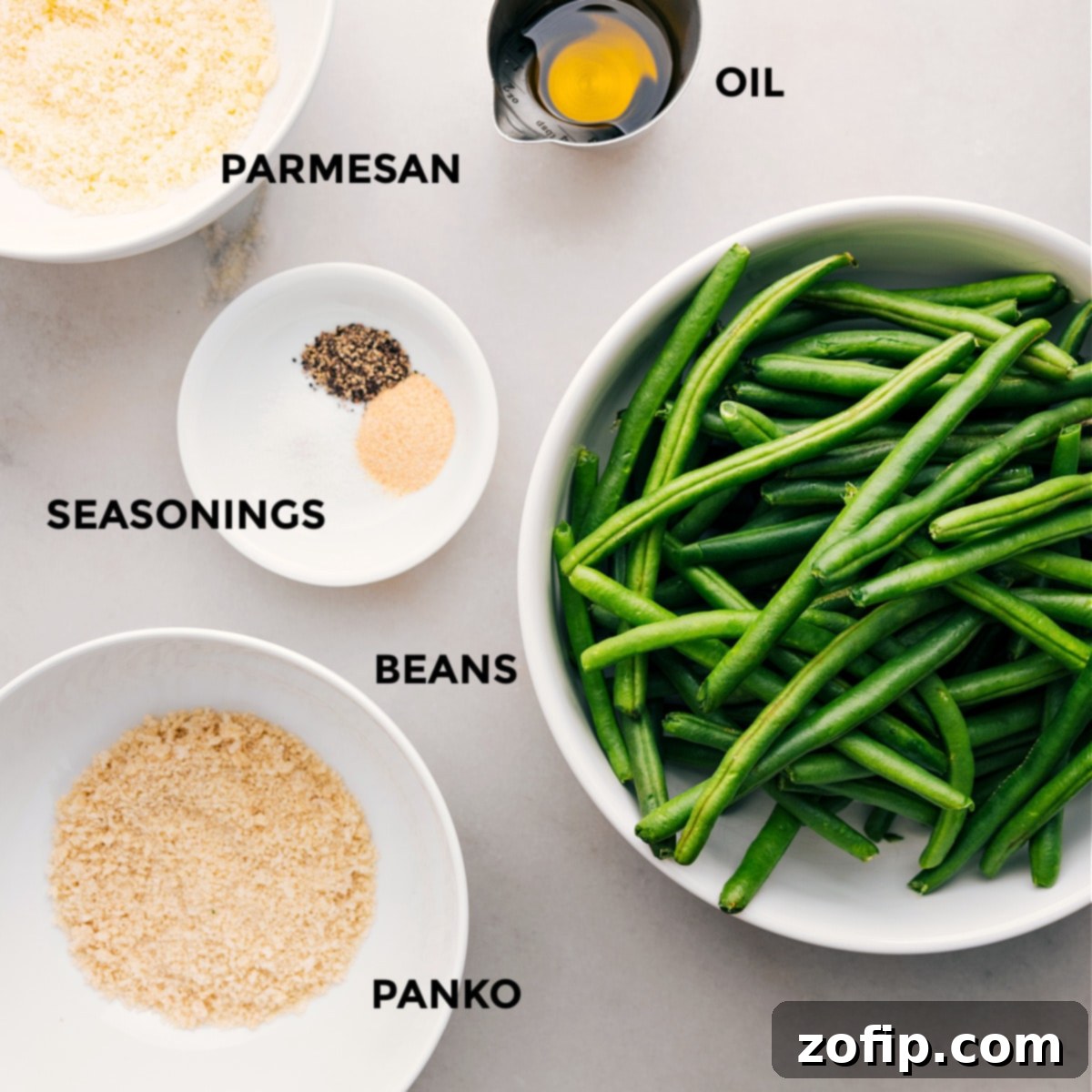 Ingredients In Roasted Green Beans (Two Ways) Arranged ingredients for roasted green beans, including fresh beans, olive oil, garlic powder, Italian seasoning, panko breadcrumbs, and grated Parmesan cheese.