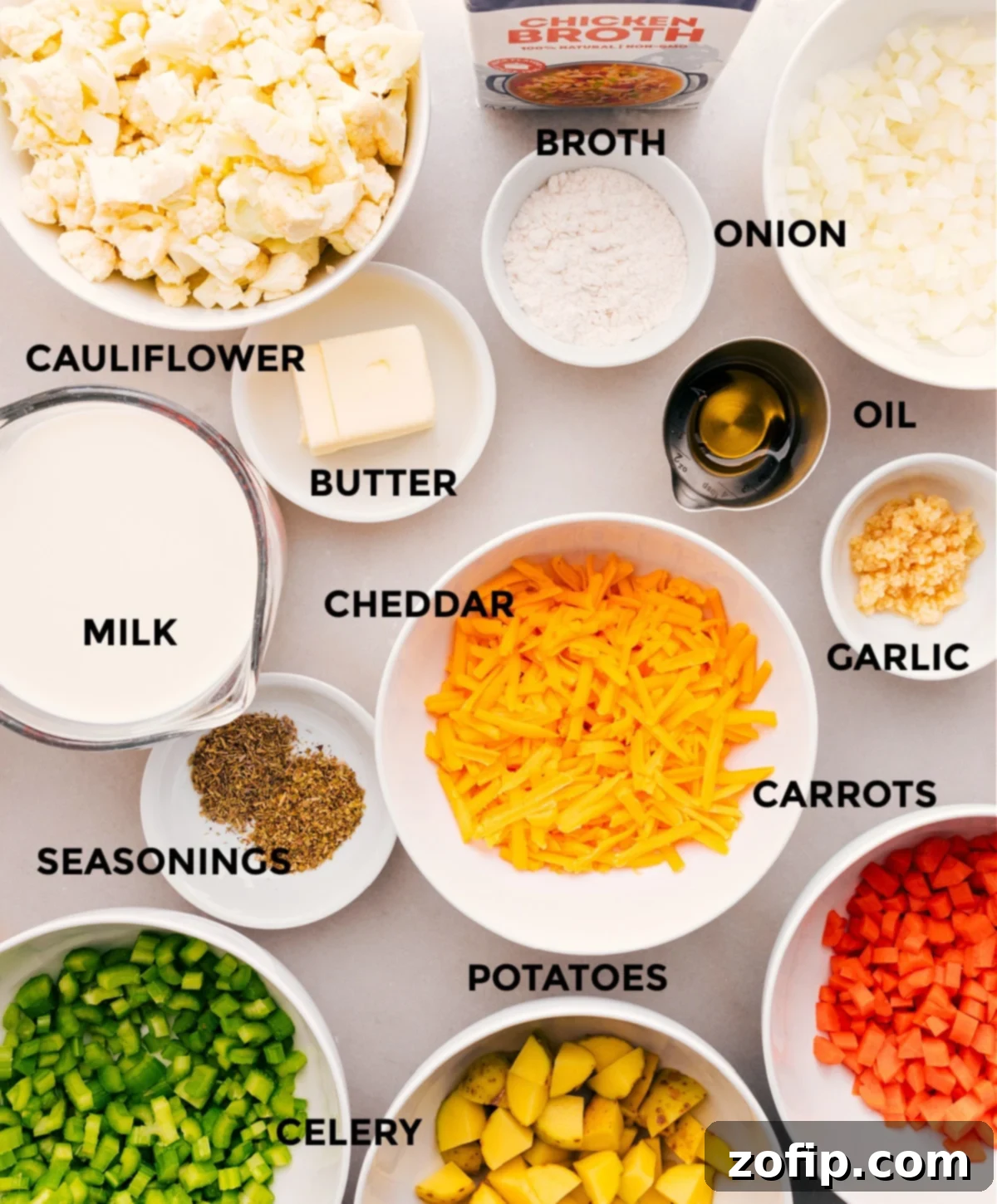 Carefully prepped ingredients for creamy cauliflower soup, including fresh vegetables, broth, butter, milk, cheddar cheese, and essential seasonings, arranged neatly for easy cooking.