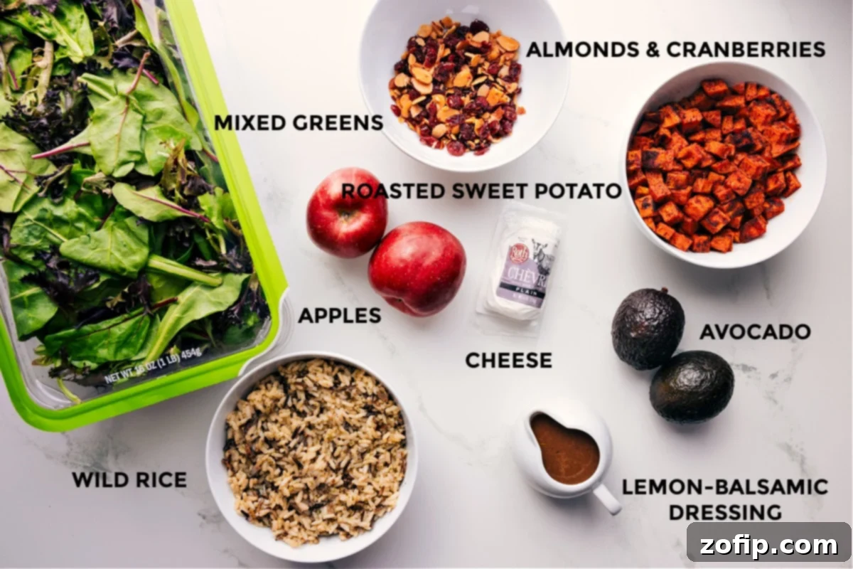 All the vibrant, fresh ingredients for the Fall Salad laid out, including a generous mix of greens, cooked wild rice, crunchy almonds, sweet cranberries, perfectly roasted sweet potato cubes, creamy avocado slices, crumbled feta cheese, and a bottle of homemade lemon balsamic dressing.