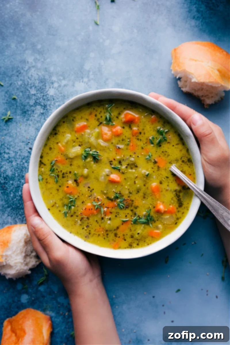Overhead image of a bowl of delicious vegetarian split pea soup, garnished with fresh herbs and a slice of bread on the side.