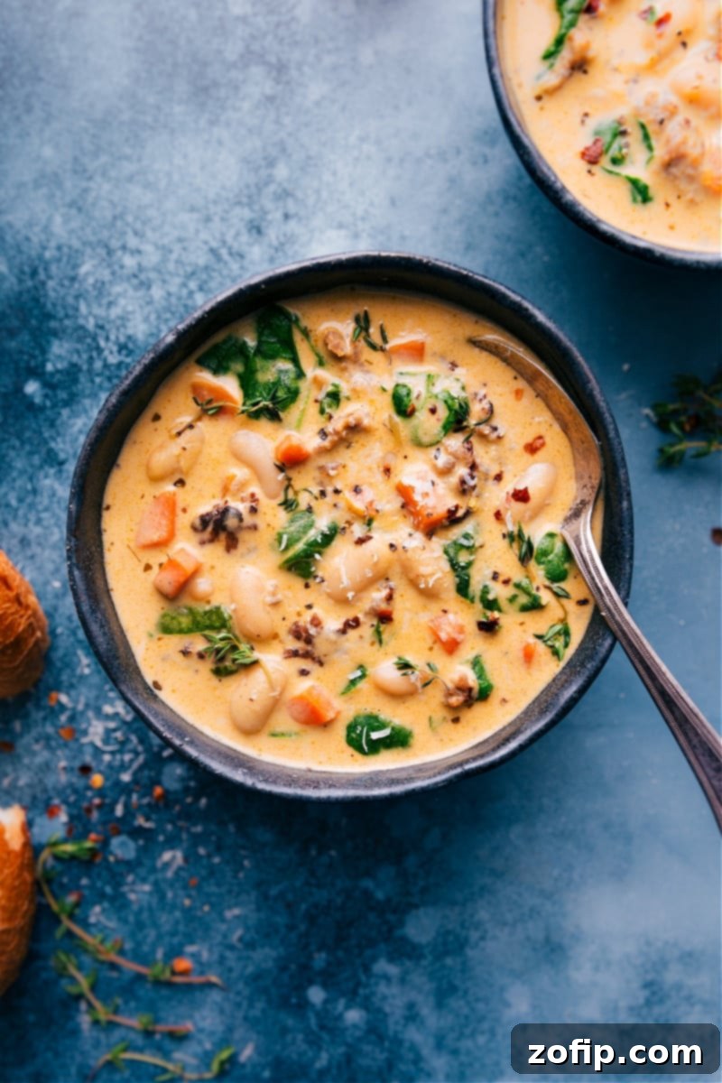 Deliciously creamy and hearty White Bean and Sausage Soup, brimming with Italian sausage, white beans, and fresh spinach, perfect for a cozy dinner. Overhead image of a large bowl of White Bean and Sausage Soup garnished with fresh herbs and a side of crusty bread, ready to be served.