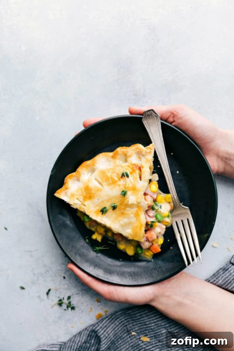 Holding a plate with this ham pot pie recipe, showcasing a generous slice with golden crust and rich filling.