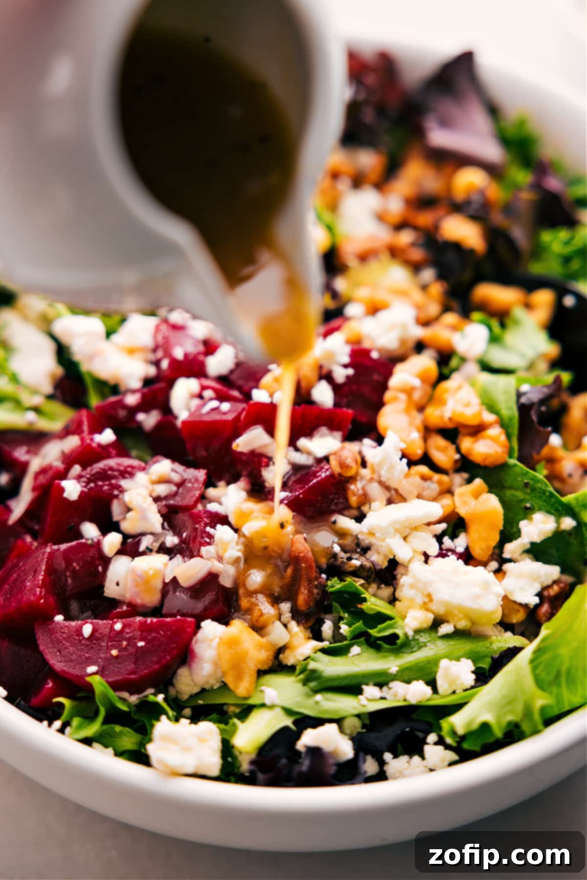 A freshly prepared Beet, Goat Cheese, and Walnut Salad being drizzled with a rich honey-Dijon dressing, ready for serving.