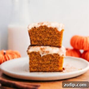 Harvest Spice Pumpkin Bars 3 Close-up of a stack of fluffy pumpkin bars topped with creamy frosting, garnished with a light dusting of cinnamon.