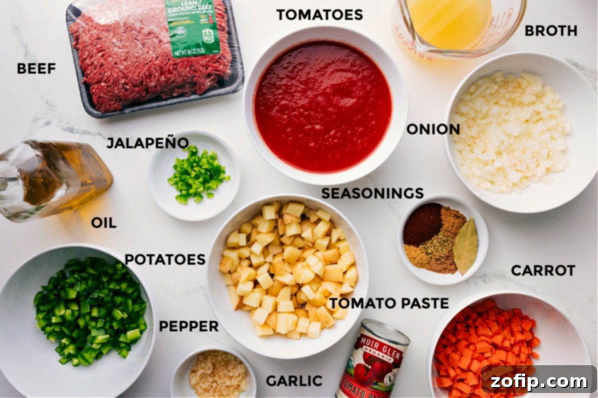 Essential Ingredients for Authentic Mexican Picadillo Recipe A vibrant array of fresh ingredients for Mexican Picadillo: lean ground beef, diced yellow onion, carrots, green bell pepper, baby gold potatoes, jalapeño, minced garlic, tomato paste, fire-roasted crushed tomatoes, chicken broth, bay leaf, and a variety of aromatic spices including salt, pepper, dried oregano, beef bouillon powder, ground cumin, ground coriander, and paprika. All components are neatly prepped and ready for cooking, highlighting the freshness and quality of the produce.