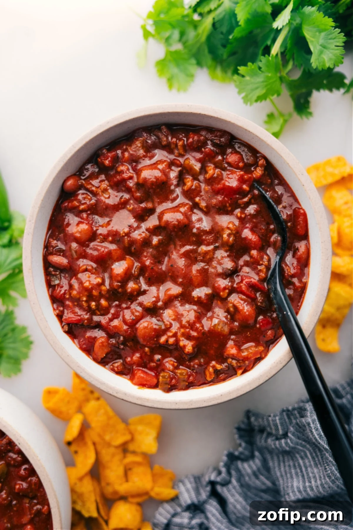 A close-up of a steaming bowl of award-winning crockpot chili, generously garnished with sour cream, shredded cheese, and fresh cilantro.