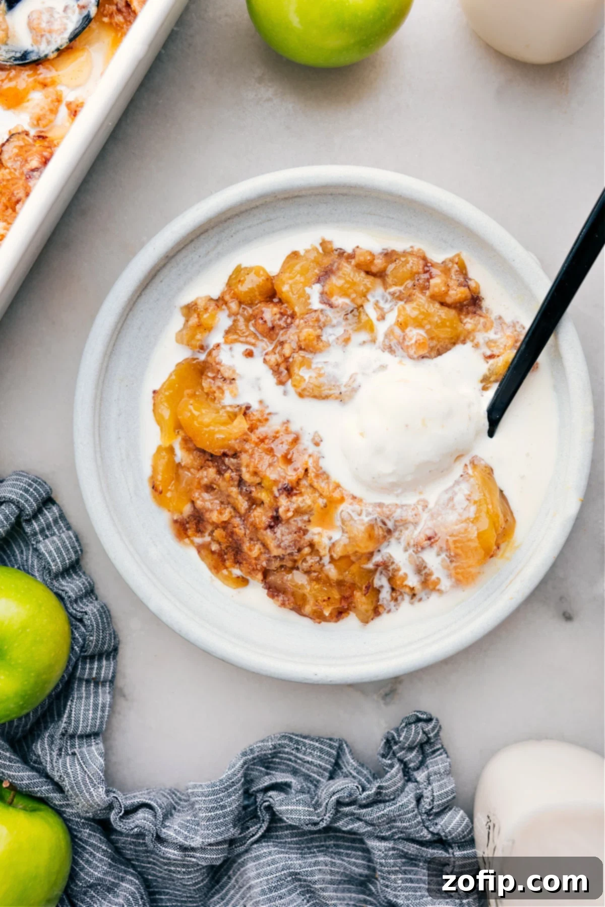 A slice of warm Apple Dump Cake on a white plate, topped with a scoop of vanilla ice cream and a drizzle of caramel.