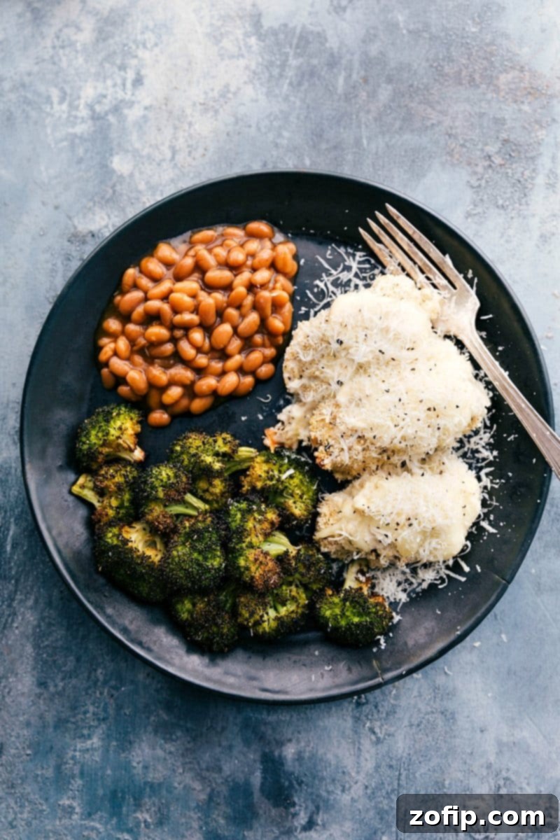 Baked alfredo chicken served on a plate with beans and roasted broccoli. The chicken is golden brown with melted white cheese on top.