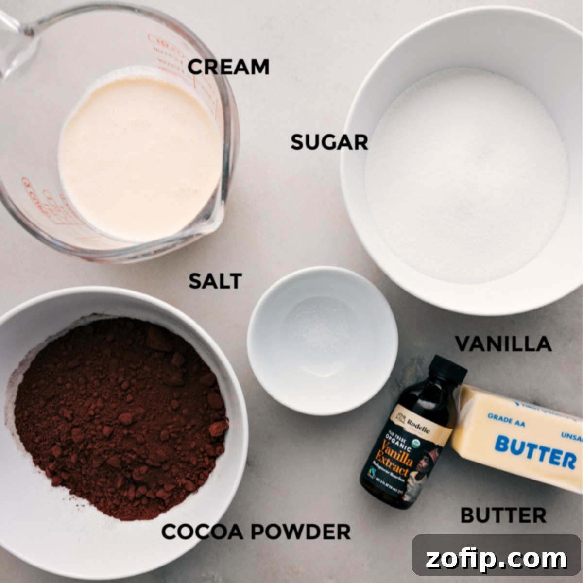 All essential ingredients for the homemade hot fudge sauce recipe are neatly arranged: granulated sugar, fine salt, rich heavy cream, premium Dutch-process cocoa powder, aromatic vanilla extract, and cubes of unsalted butter.