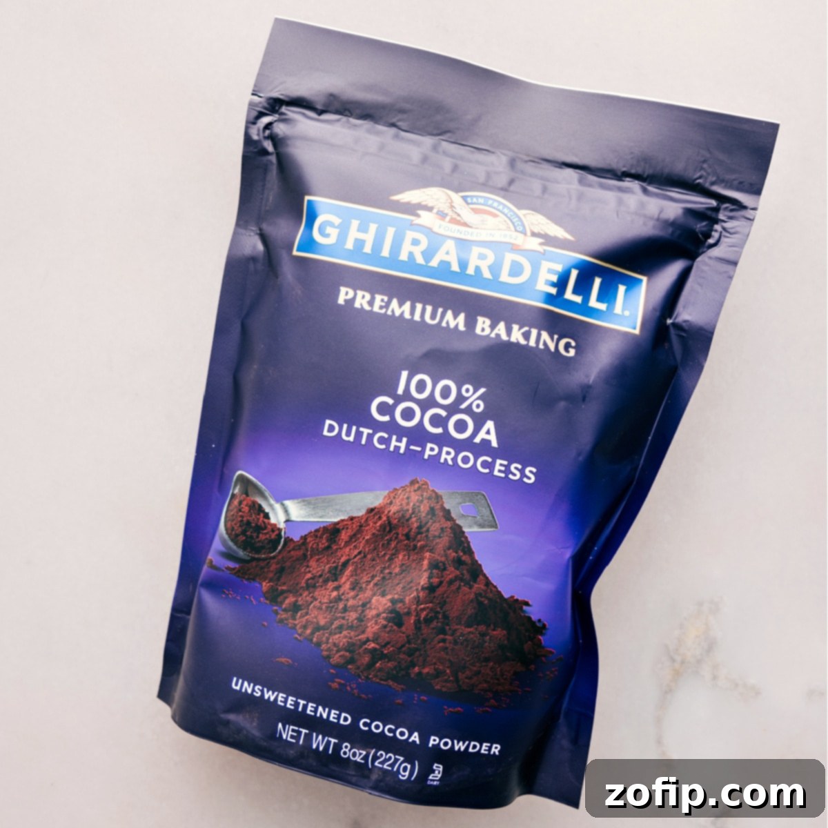 A close-up of Dutch-process cocoa powder, a key ingredient for the hot fudge sauce, emphasizing its fine texture and deep color.