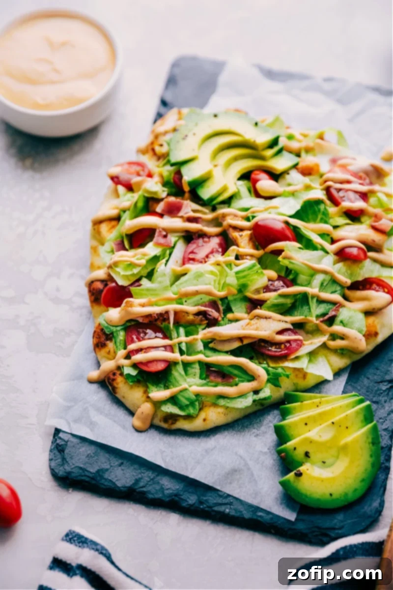 Chipotle Chicken Flatbread featuring naan, rotisserie chicken, pepper-jack cheese, avocado, lettuce, tomatoes, bacon, and chipotle ranch dressing.