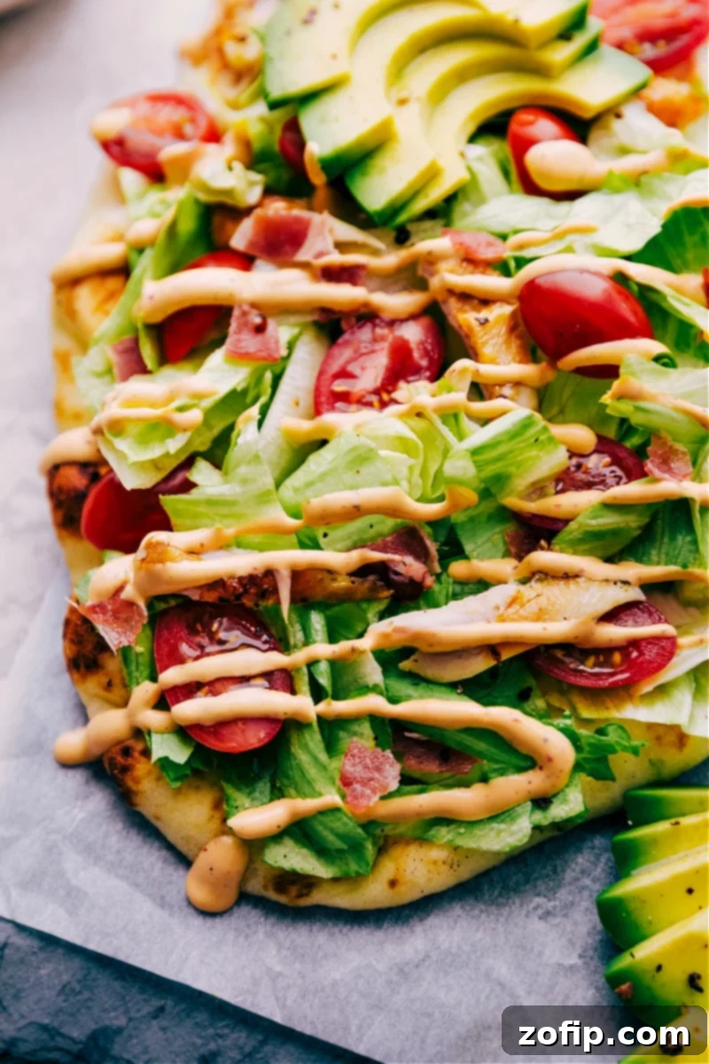 A close-up shot of a finished Chipotle Chicken Flatbread, showcasing the rich textures and colors of the chicken, cheese, avocado, and dressing on naan.