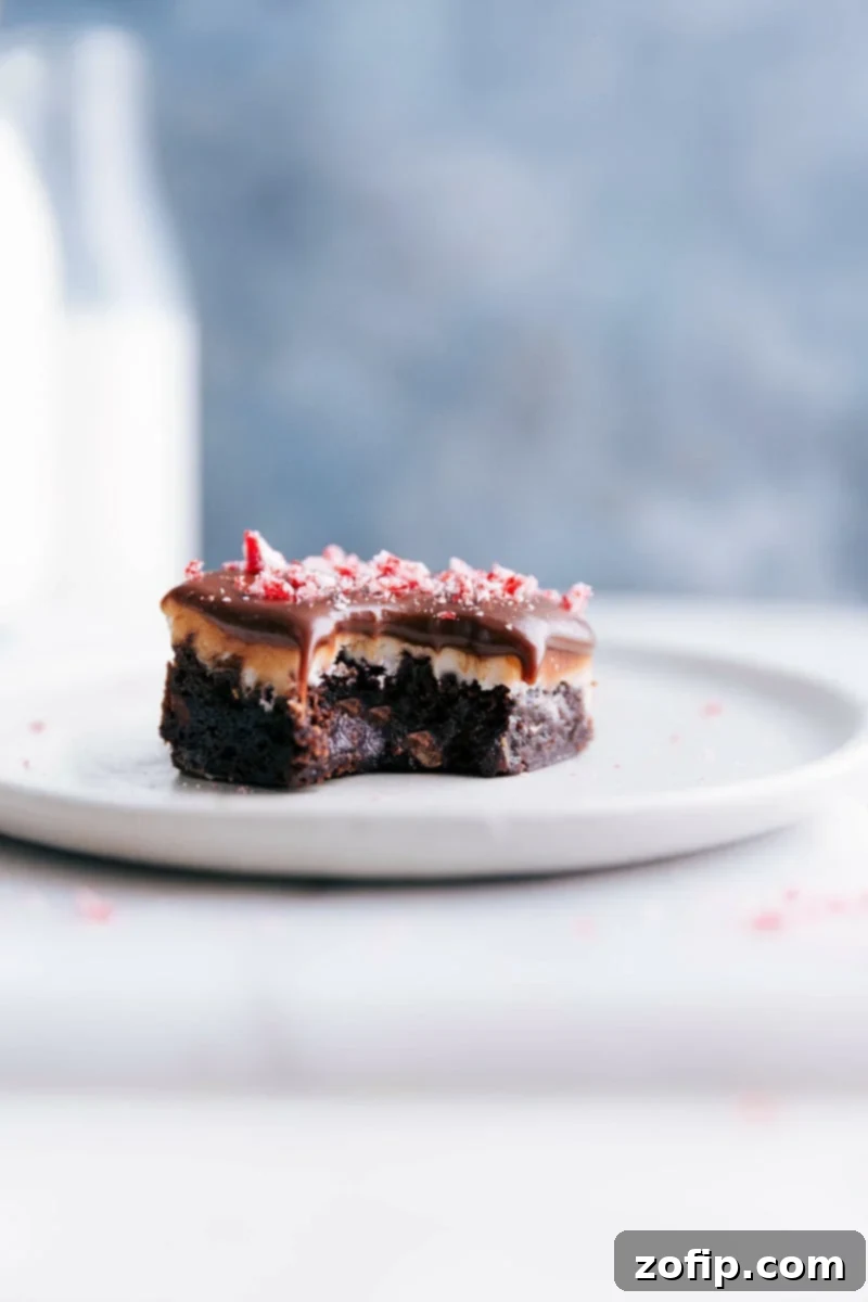 Tempting Bite Reveals Peppermint Frosting and Chocolate Ganache of Decadent Brownie A luscious peppermint brownie with a bite mark, showcasing its peppermint frosting and rich chocolate ganache topping, presented on a plate.