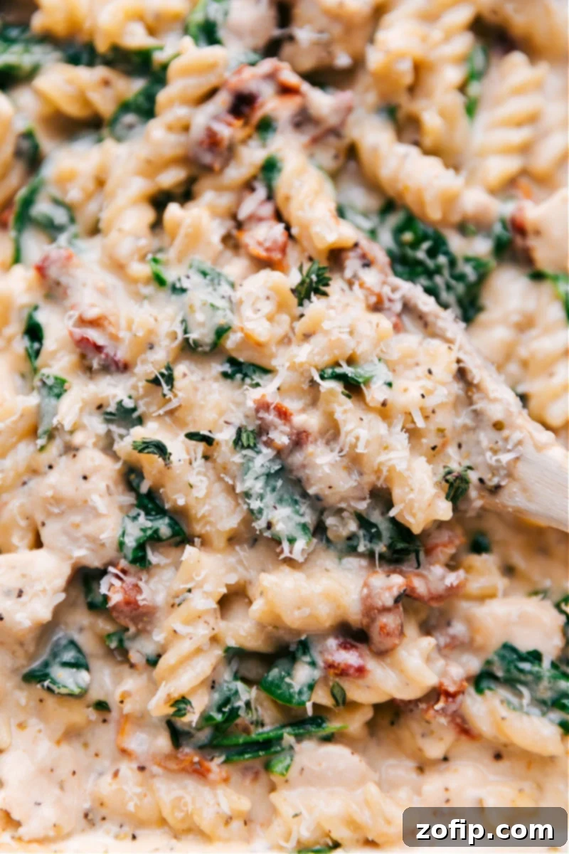 Overhead image of Tuscan Chicken Pasta, showcasing its creamy sauce, rotini pasta, chicken pieces, and vibrant spinach and sun-dried tomatoes.