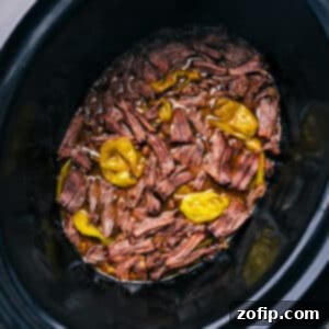 Close-up of shredded Mississippi Pot Roast with gravy in a slow cooker.
