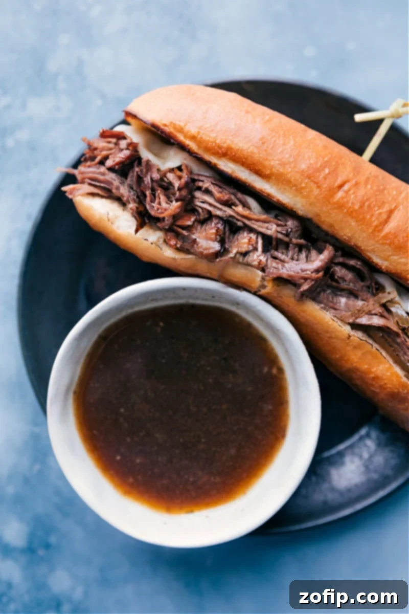 A perfectly assembled French Dip Sandwich with tender beef and melty cheese on a toasted garlic roll, ready to be dipped into a small bowl of savory au jus.